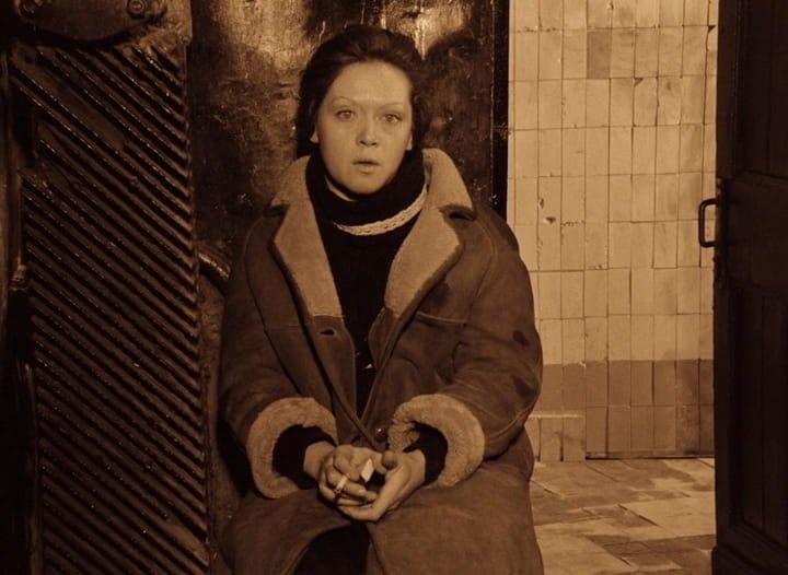Em sépia, a mulher do Stalker (Alisa Freindlich), sentada junto a uma parede de azulejos, fala olhando para a câmera, em Stalker (1979), de Andrei Tarkóvski.