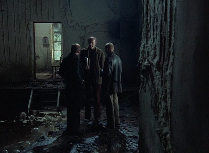 O Escritor (Anatoli Solonítsin), o Stalker (Aleksandr Kaidanóvski) e o Professor (Nikolai Grinko), de gorro, num corredor escuro e úmido, em Stalker (1979), de Andrei Tarkóvski.